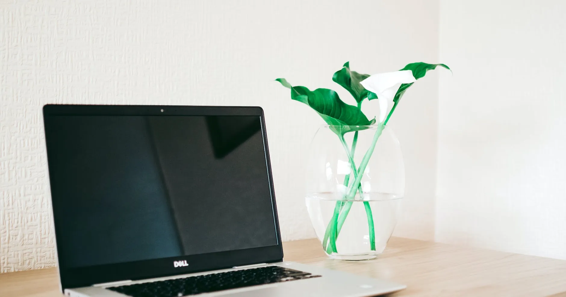 silver and black dell laptop beside white calla lily in clear glass vase on brown wooden desk
