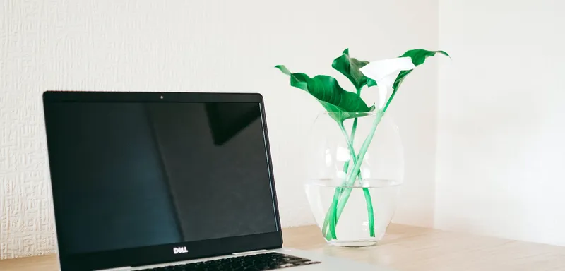 silver and black dell laptop beside white calla lily in clear glass vase on brown wooden desk